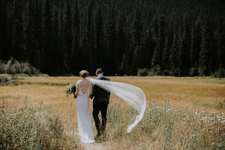 a bride and groom walk away through strawberry flats, her veil blows In the wind