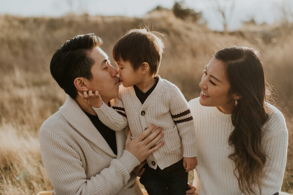 a little boy kisses his dad while the mom watches