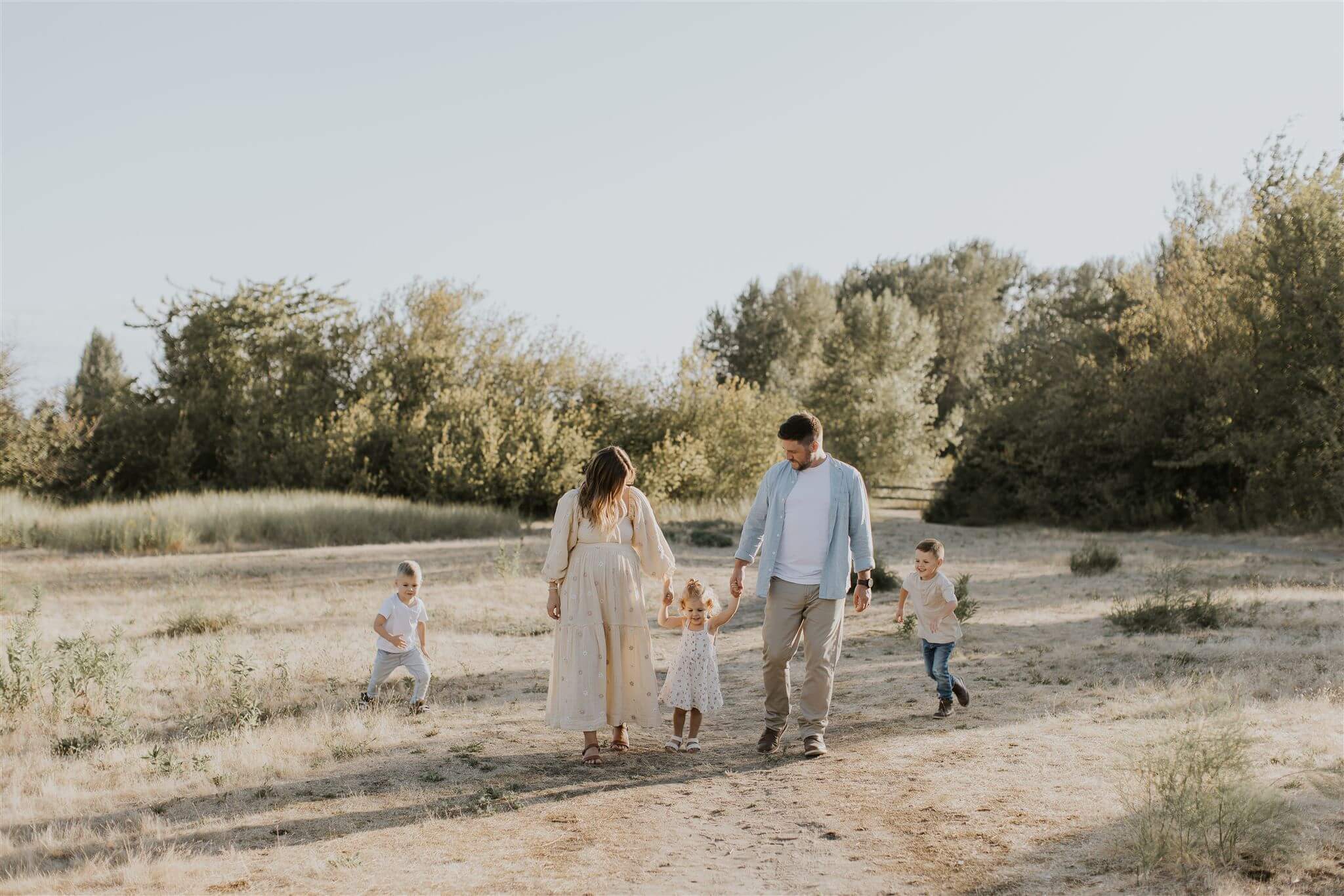 family walking through a field in the summer, the smallest kid is being swung into the air