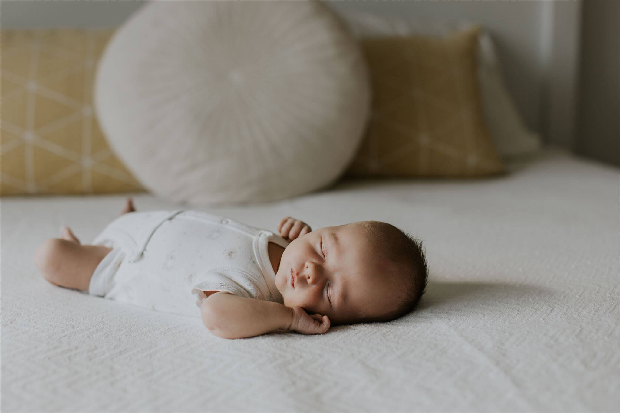 a newborn baby lays on a bed with his hand under his head