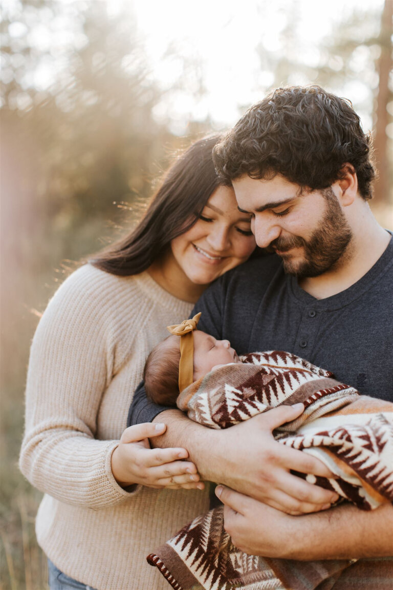 new parent smile down at their baby while the sun shines through the tress at their Cranbrook acreage.