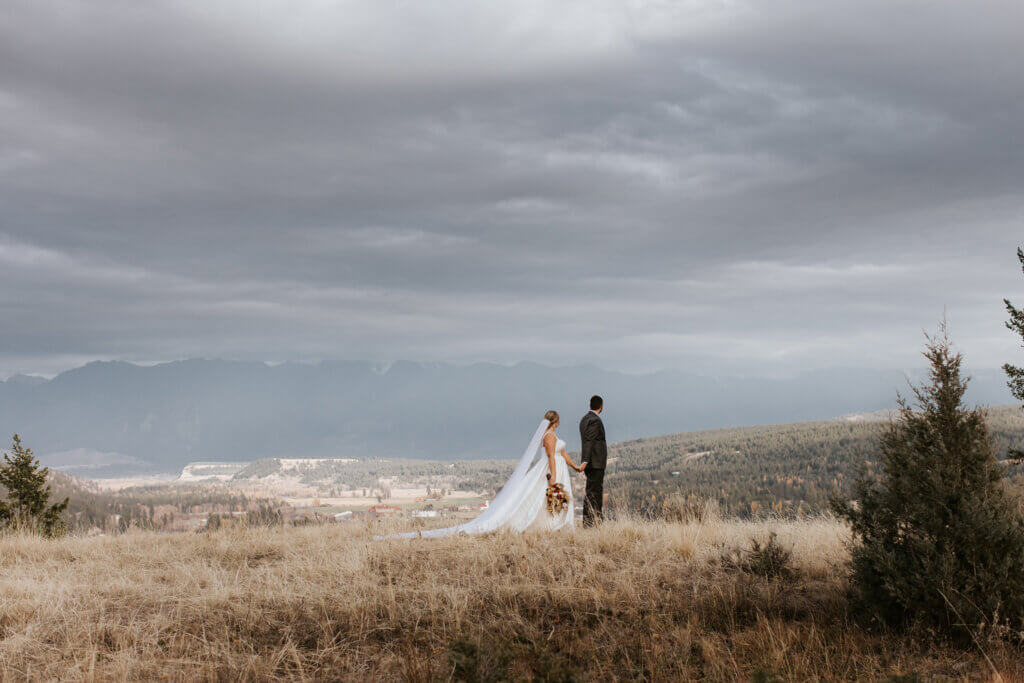 A bride and groom walk and look off at the Rockies in Cranbrook, BC