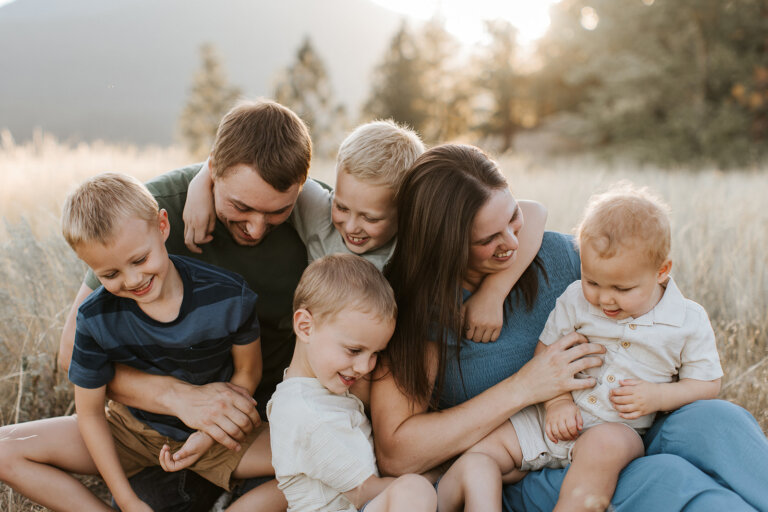 a family with four young boys laughing in a field near Kimberley, BC