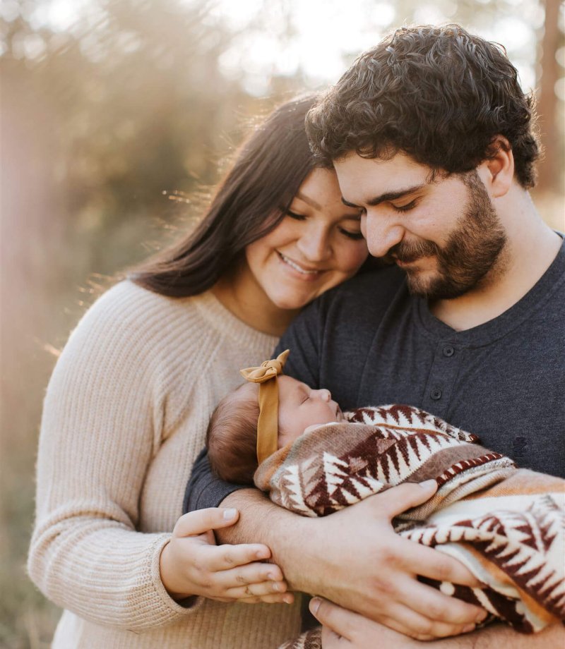 new parent smile down at their baby while the sun shines through the tress at their Cranbrook acreage.