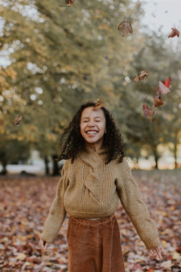 a is smiling and throwing fall leaves in the air