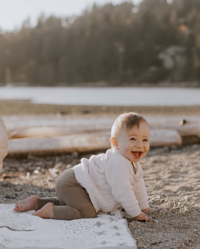 a ten month old boy crawling and smiling at the beach