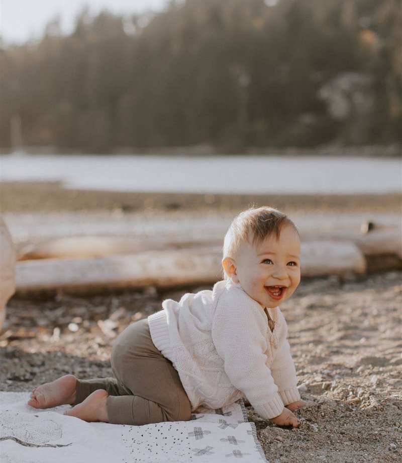 a ten month old boy crawling and smiling at the beach