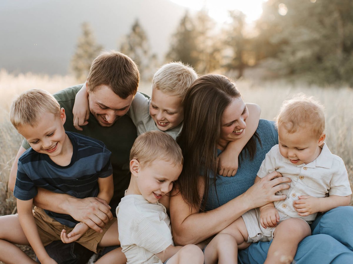 a family with four young boys laughing in a field near Kimberley, BC